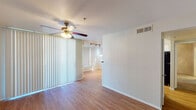 This single-floor residence offers a thoughtfully laid-out living space with a blend of functional design and comfortable finishes throughout. The entry opens into a bright living area featuring warm wood-look flooring, a ceiling fan with light fixture, and large vertical blinds that invite natural light while providing privacy. Track lighting in the adjoining area adds a layer of versatile illumination as the space flows toward the kitchen.

The kitchen is well-appointed with white cabinetry, dark granite-style countertops, and black appliances including a gas range, built-in microwave, refrigerator, and dishwasher. A breakfast bar peninsula provides additional counter space, and the wood-look flooring continues seamlessly through this area. A hallway connects the kitchen to the rest of the unit, maintaining a practical and open circulation path.

The bedrooms are carpeted for comfort and each features a ceiling fan with lighting. The primary bedroom is notably spacious, offering direct access to both an en-suite bathroom and a walk-in closet, providing generous storage. A second bedroom also includes a ceiling fan and vertical blinds for light control. Throughout the residence, neutral wall tones and clean white trim create a cohesive, move-in-ready atmosphere.