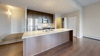 Located at 1515 W 57th Ave in Vancouver, BC, this well-appointed two-storey home offers 2 bedrooms and 2 bathrooms across two thoughtfully laid-out floors. The space is designed with a contemporary aesthetic, blending clean lines and modern finishes throughout.

The kitchen is a standout feature, showcasing rich dark-wood cabinetry, a generous island with a crisp white countertop and undermount sink, and a full suite of stainless steel appliances including a refrigerator, range, and built-in microwave. Warm hardwood flooring anchors the kitchen and flows seamlessly through the main living areas.

Both bedrooms are carpeted and bathed in natural light through large floor-to-ceiling windows that frame views of the surrounding neighbourhood's greenery. The primary bedroom includes a mirrored sliding-door closet as well as an additional storage nook. The second bedroom offers equally generous proportions and outdoor views.

The two bathrooms are finished in a modern style — one features dark wood cabinetry, a white undermount sink, wall-mounted mirror with a floating shelf, and stylish lighting, while the second is clean and functional with neutral tile flooring.

Connecting the two floors are staircases that pass through well-proportioned hallways, ensuring smooth circulation throughout the home. The overall ambiance is bright, modern, and functional.