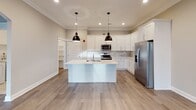 Located on Scholar Lane in Forest, Virginia, this single-floor residence offers a well-designed layout with a clean, contemporary aesthetic throughout. The kitchen serves as a central highlight, showcasing crisp white shaker-style cabinetry extending to the ceiling, stainless steel appliances including a range, microwave, and refrigerator, a marble-style tile backsplash, and light quartz countertops. A central island with pendant lighting overhead and light wood-tone flooring adds both function and style to the space. The open living area features elegant crown molding, recessed lighting, a ceiling fan, and a distinctive arched entryway with double doors topped by a transom window, allowing natural light to fill the room. Bedrooms are finished with plush carpeting, neutral-toned walls, and ample closet storage with built-in shelving and hanging rods. Natural light flows through large windows fitted with blinds. The bathrooms are finished with stone-look tile flooring, white vanities with quartz countertops, and tub-shower combinations with chrome fixtures. Connecting hallways are carpeted and lead seamlessly between rooms, contributing to the home's cohesive and comfortable feel.