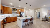 This thoughtfully designed single-floor residence combines contemporary style with functional living. At its heart is a spacious, open-concept kitchen outfitted with warm honey-toned wood cabinetry, stainless steel appliances, a classic white subway tile backsplash, and generous quartz countertops. A substantial kitchen island with seating for two provides an ideal casual dining or gathering space, illuminated by a trio of elegant glass pendant lights. Open shelving adds a modern, accessible touch to the cabinetry layout.

The living area is bright and inviting, featuring large sliding glass doors that welcome natural light and provide access to the outdoors. The space flows seamlessly from the kitchen into the dining and living areas, creating a cohesive, connected feel throughout.

The bedrooms are comfortably proportioned, each featuring plush carpeting, ceiling fans, and windows that bring in natural light. The bathrooms echo the home's consistent design language, with matching wood vanities, quartz countertops, and tile flooring.

Light wood-look flooring runs throughout the main living spaces, tying the home together with a clean, modern aesthetic. Neutral wall tones and recessed lighting create a warm, well-lit ambiance across every room, making this residence as practical as it is visually appealing.
