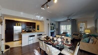 This well-appointed single-floor residence showcases a thoughtfully designed open-concept layout that seamlessly connects the main living spaces. The kitchen is outfitted with dark espresso cabinetry, stainless steel appliances including a refrigerator, range, and microwave, and a light granite countertop with a breakfast bar that flows into the dining area. The dining space features a round glass-top table with contemporary white chairs, illuminated by stylish track lighting overhead and natural light from large windows. Rich hardwood-style flooring runs throughout the main living areas, adding warmth and continuity. The living room is bright and inviting, with a ceiling fan, large sliding glass doors that open to a private balcony overlooking lush greenery, and ample space for comfortable seating arrangements. The bedrooms offer a serene retreat; the primary bedroom features teal accent walls, hardwood-style floors, natural light from large windows, and a dark wood dresser, while a secondary bedroom presents a clean, bright aesthetic with neutral tones and an upholstered headboard. Bathrooms are well-finished, with one featuring a soaking tub and light blue walls, and another boasting a double-sink vanity with vessel sinks and marble-style countertops. Overall, the space presents a cohesive, modern aesthetic throughout.