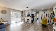 This well-designed one-bedroom, one-bathroom unit in Austin, TX offers a smartly utilized floor plan that maximizes every square foot. Wood-look flooring runs throughout the entire space, providing a cohesive and modern aesthetic. The open-concept kitchen and living area serves as the heart of the unit, anchored by a peninsula with bar seating that creates a natural divide between cooking and living spaces. The kitchen is equipped with gray cabinetry, black appliances, a mosaic tile backsplash, light countertops, and a double-basin sink — combining both function and style. A wall of built-in shelving flanks a full-height sliding glass door in the living area, which floods the space with natural light and provides direct outdoor views. The bedroom is a comfortable retreat featuring a ceiling fan, a window with natural light, and generous closet storage including a walk-in closet and an additional shelved closet. The bathroom features gray cabinetry, a dark granite countertop, a large framed mirror, and wood-look tile flooring. Textured ceilings are present throughout, and the overall layout is efficient and functional, making this unit an ideal choice for those seeking a practical yet stylish home in Austin.