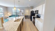 This single-floor residence offers a thoughtfully designed open layout with a neutral color palette of soft grays and warm beiges throughout. The kitchen serves as a central highlight, featuring granite-style countertops, white shaker cabinetry, a double-basin undermount sink, and black appliances including an electric range, microwave, and refrigerator. Pendant lighting and light wood-style flooring enhance the space, which flows seamlessly into the living area. A built-in desk nook adjacent to the kitchen provides a dedicated workspace.

The dining area is bright and airy, benefiting from a sliding glass door that opens onto a private balcony, allowing natural light to fill the room. Multiple bedrooms offer carpeted flooring, ceiling fans, and windows fitted with blinds for light control. Each bedroom provides a comfortable, functional retreat.

Two full bathrooms are finished with granite-topped white vanities, light wood-style flooring, and tub-shower combinations. One bathroom features a shower curtain setup, while the other includes a tiled surround. The overall design maintains a consistent, clean aesthetic that balances practicality with modern residential style.