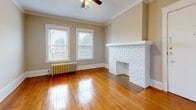 Located at 12933 Clifton Blvd in Lakewood, Ohio, this one-bedroom, one-bathroom unit offers a blend of classic architectural charm and functional layout across a single floor. The living room serves as the focal point of the space, showcasing rich hardwood floors, elegant crown molding, and a white-painted brick fireplace that adds character and warmth. Two windows allow natural light to fill the room, while a ceiling fan and cast-iron radiator provide year-round comfort. The bedroom mirrors this classic aesthetic with the same gleaming hardwood floors, crown molding, a ceiling fan, and a radiator beneath a bright window. The kitchen is efficiently designed with warm oak cabinetry, dark countertops, a white gas range, a stainless steel sink, and a clean white subway tile backsplash. Stone-look tile flooring extends through the kitchen and into the hallway, connecting to a pantry and closet for added storage. The bathroom features a full tub-shower combination with a white surround. Throughout the unit, neutral warm-toned walls and consistent trim work create a cohesive and timeless interior, reflecting the enduring character typical of Lakewood's historic residential architecture.