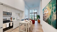 Located at 303 South Federal Highway in Hollywood, FL, this modern one-bedroom, one-bathroom residence offers a thoughtfully designed open-concept layout across a single floor. The living and kitchen areas flow seamlessly together beneath dramatically soaring ceilings, creating an airy, loft-like atmosphere that feels expansive. Light wood flooring runs throughout, complementing the bright white walls and abundant natural light.

The kitchen is outfitted with flat-front cabinetry in a soft gray finish, stainless steel appliances including a refrigerator, range, microwave, and dishwasher, and clean white countertops. A compact kitchen island provides additional prep space and casual seating. The living area is anchored by floor-to-ceiling glass doors that open to an outdoor view of lush landscaping, flooding the space with natural light.

The bedroom is a calm, well-proportioned retreat with tall windows overlooking greenery, offering a serene outdoor connection. Two closets provide generous storage. The bathroom features a clean, minimalist design with a white vanity and light wood-toned flooring. In-unit laundry adds everyday convenience. Part of a modern mid-rise building, this residence combines contemporary finishes with a prime South Florida location.