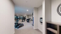 Located at 1850 Glenview Rd in Glenview, Illinois, this fitness center offers a spacious, single-floor exercise room designed to support a full range of workout routines. The room is finished with neutral gray walls and plush carpeted flooring, creating a clean and comfortable environment conducive to exercise.

The space is generously appointed with a diverse selection of equipment. Cardio offerings include multiple True-brand treadmills, elliptical trainers, recumbent bikes, and a stair climber, all positioned near large windows that flood the area with natural light and provide views of the surrounding exterior. For strength training, the room features a multi-station cable machine, a leg press, adjustable benches, and a dedicated free-weight area with a full dumbbell rack. A wall-mounted flat-screen television and full-length mirrors enhance both the functionality and the sense of openness within the space.

Recessed lighting throughout the ceiling ensures the room is well-lit during all hours, while a separate utility room door is accessible from within the exercise area. The layout is thoughtfully organized to allow ample circulation between equipment, making the space practical for multiple users simultaneously. Overall, this fitness center delivers a professional, amenity-rich environment suited for a broad spectrum of fitness activities.