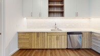 Located at 3009 W Leigh St in Richmond, Virginia, this single-floor unit offers a thoughtfully designed contemporary layout with a cohesive blend of modern finishes and functional living spaces. The open-concept living and kitchen area is anchored by warm hardwood-style flooring, recessed lighting, and large windows that invite natural light into the space. The kitchen is a standout feature, equipped with a full suite of stainless steel appliances including a range, over-the-range microwave, refrigerator, and dishwasher. Two-toned cabinetry pairs white upper cabinets with wood-grain lower cabinets, complemented by clean white quartz countertops, a subway tile backsplash with under-cabinet lighting, and open shelving for additional storage. The bedrooms feature soft carpeting and ceiling fans, with windows offering exterior views. Two bathrooms serve the unit: one features a floating wood-tone vanity, large-format white tile flooring, and a glass-enclosed walk-in shower with tile surround, while the second offers a soaking tub with a tiled surround and a built-in niche. The overall aesthetic is clean, bright, and modern, making this a well-appointed space in a vibrant Richmond neighborhood.