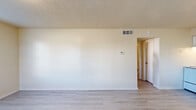 This efficient single-floor unit offers a well-organized layout comprising one bedroom, one bathroom, and a full kitchen. Throughout the space, light gray laminate flooring provides a clean, cohesive look, while neutral wall tones create a bright and airy atmosphere. Textured popcorn ceilings are consistent across the living areas and bedroom.

The living area features white walls, ceiling-mounted HVAC vents, and a thermostat, lending a functional, move-in-ready feel. The kitchen is equipped with white cabinetry—both upper and lower—alongside a white electric range, a double-basin sink with an under-cabinet range hood, and a full-size refrigerator. A window in the kitchen dining area allows natural light to filter in, making it a pleasant spot for casual meals.

The bedroom is a comfortable size, featuring a window with horizontal blinds that brings in natural light. A built-in closet with a full-length hanging rod provides practical storage. The bathroom includes a tub-and-shower combination with white tile surround and safety grab bars installed for added accessibility, alongside a standard toilet. Overall, the unit delivers a straightforward and functional living environment with clean finishes throughout.