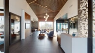 This thoughtfully designed amenity space delivers a refined, hotel-inspired atmosphere across a single expansive floor. The grand lobby immediately establishes the tone, showcasing soaring ceilings adorned with a striking slatted wood canopy, large-format dark tile flooring, and cascading globe pendant chandeliers. Floor-to-ceiling windows flood the space with natural light, while a sculptural geometric accent wall and a reception desk anchor the entry.

The main lounge area features a dramatic floor-to-ceiling fireplace clad in dark paneling with gold inlay detailing, surrounded by plush leather seating and marble-topped coffee tables. An adjacent media lounge offers a large multi-screen display wall paired with iconic egg-style chairs and casual seating arrangements set atop warm hardwood flooring.

A vibrant social kitchen and dining area features bold geometric tile flooring in gold and teal tones, sleek dark cabinetry, a full kitchenette, and bistro-style seating throughout. A private conference room provides a polished work setting with a long white table, bold orange chairs, and a large wall-mounted display, illuminated by distinctive glass globe pendant fixtures. Together, these zones create a cohesive, contemporary environment ideal for both socializing and productivity.