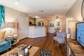 Located at 1700 S Araby Dr in Palm Springs, CA, this single-story residence offers a well-designed layout that balances comfort and functionality. Rich hardwood flooring flows throughout the main living areas, creating a warm and cohesive aesthetic.

The living room serves as the heart of the home, featuring recessed lighting, a large sliding glass door with vertical blinds that invite natural light and provide access to the outdoor area. A bold teal abstract artwork anchors one wall, complementing the eclectic furnishings that include a woven coffee table, colorful media console, and patterned area rug.

The kitchen is well-appointed with light wood cabinetry, granite countertops with a breakfast bar, stainless steel appliances including a gas range and refrigerator, and a window that keeps the space bright and airy.

The bedroom offers a calm retreat with plush carpet flooring, a generously sized window overlooking lush outdoor greenery, and warm ambient lighting. The bathroom is clean and functional, featuring a full tub and shower combination with wood-toned flooring that ties into the home's overall design palette.

Throughout the residence, neutral wall tones and consistent finishes create a cohesive, inviting atmosphere well-suited to the sunny Palm Springs lifestyle.