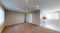 Located at 6200 Edinger Ave in Huntington Beach, California, this single-story residence offers a clean, modern aesthetic throughout. The open living area is finished with wall-to-wall carpet, neutral gray walls, and recessed lighting, creating a bright and welcoming atmosphere. The space flows seamlessly into the kitchen, which features white shaker-style cabinetry, dark countertops, wood-look flooring, and a full suite of stainless steel appliances including a gas range, over-the-range microwave, dishwasher, and single-basin sink. The bedrooms are carpeted and generously proportioned, each featuring ceiling fans and mirrored sliding closet doors that maximize both storage and the sense of space. One bedroom includes a built-in shelving system within the closet, offering organized storage solutions. A window with vertical blinds brings in natural light and frames views of palm trees and surrounding greenery. The bathroom is finished with wood-look flooring, white cabinetry with dark countertops, a well-lit vanity mirror, and a tub-shower combination. Consistent use of neutral tones, recessed lighting, and modern hardware throughout the home creates a cohesive and functional living environment well-suited to the Southern California lifestyle.