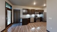 Located at 4930 Founders Terrace in Green Bay, Wisconsin, this efficiently designed single-floor unit makes excellent use of its footprint. Light-toned wood-style flooring runs throughout, creating a cohesive and easy-to-maintain aesthetic that ties each area together seamlessly.

The kitchen is a standout feature, outfitted with rich, dark espresso cabinetry extending to the upper and lower walls, offering generous storage. A full suite of stainless steel appliances — including a refrigerator, electric range, microwave, and dishwasher — provides all the essentials for daily cooking. Light-toned countertops and a classic tile backsplash complete the clean, modern look.

A hallway connects the main living area to the entry door, with a wall-mounted thermostat and recessed lighting adding practical touches to the space. The bathroom is thoughtfully appointed, featuring a dark-toned vanity with a granite-style countertop, an undermount sink, a framed mirror, and accessibility-friendly grab bars. Neutral gray walls and coordinating flooring give the bathroom a calm, polished feel.

The dedicated closet provides functional storage through multi-tiered wire shelving systems mounted along the walls, maximizing vertical space. Overall, the unit presents a modern, neutral palette with consistent finishes, making it a practical and comfortable living space.