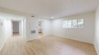 This single-story, 1-bedroom, 1-bathroom unit offers a clean, efficient layout spanning a comfortable living footprint. Throughout the space, light hardwood-style flooring provides a warm, cohesive look that ties each room together. The open living room is bathed in natural light from a large window with blinds, complemented by a textured ceiling and crisp white walls that create a bright, airy atmosphere. A panel heater is conveniently located in the living area for year-round comfort. The kitchen is well-equipped with stainless steel appliances, including an electric range, over-the-range microwave, and dishwasher, alongside light-toned cabinetry with gold hardware and a built-in sink beneath a window. The generously sized bedroom features a textured ceiling, a window overlooking greenery, and direct access to a dedicated walk-in closet outfitted with full-length hanging rods and shelving. The bathroom includes a tiled shower-tub combination, a toilet, and a dark navy vanity with gold hardware accents, offering a stylish contrast to the otherwise neutral palette. A hallway connects the main living areas and provides additional utility access. The unit's consistent use of light tones and modern finishes throughout creates a clean, move-in-ready environment.