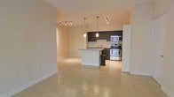 This single-floor space offers a clean, contemporary design with an open-concept layout that connects the living area and kitchen in a seamless, functional arrangement. The kitchen is a standout feature, showcasing dark espresso cabinetry that contrasts elegantly with light granite countertops and a classic subway tile backsplash. A central island provides additional prep space and serves as a natural divider between the kitchen and living areas. Stainless steel appliances — including a double oven range, built-in microwave, and additional cooking appliances — add a polished, modern touch. Pendant lighting hangs above the island, complementing the track lighting installed throughout the open living and kitchen zones, ensuring the space is well-lit at all times. Large-format, light-toned tile flooring runs continuously throughout, lending a sense of spaciousness and cohesion to the interior. The warm, neutral wall tones enhance the bright, airy ambiance of the space. Crisp white baseboards and door trims provide clean architectural definition. Overall, the space delivers a practical yet stylish environment well-suited for modern everyday living.