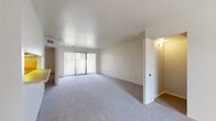 This single-floor residence offers a clean, functional layout designed for comfortable everyday living. The living area is generously sized, finished with soft wall-to-wall carpeting and neutral walls that create a bright, open atmosphere. A sliding glass door dressed with vertical blinds allows natural light to fill the space and provides access to the outdoors. A pass-through opening connects the living area to the kitchen, maintaining an open flow between the two spaces.

The kitchen is well-equipped with cream-toned cabinetry featuring wood-trim accents, a full-size refrigerator, an electric range with oven, a dishwasher, and ample counter space. The hard-surface flooring in the kitchen provides a practical contrast to the carpeted living areas.

The bedroom is a comfortable retreat, carpeted and bathed in natural light from a large window with vertical blinds. It includes a walk-in closet, offering generous storage. An additional room with a sloped ceiling and hard-surface flooring provides flexible use as a storage or utility space.

Two bathrooms serve the residence. The primary bathroom features a tub-shower combination with tile surround, a wide vanity with an integrated sink, and a large mirror with overhead lighting. The second bathroom offers a similarly clean design with a single vanity and mirrored medicine cabinet.