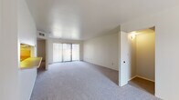 This single-floor residence offers a clean, functional layout designed for comfortable everyday living. The living area is generously sized, finished with soft wall-to-wall carpeting and neutral walls that create a bright, open atmosphere. A sliding glass door dressed with vertical blinds allows natural light to fill the space and provides access to the outdoors. A pass-through opening connects the living area to the kitchen, maintaining an open flow between the two spaces.

The kitchen is well-equipped with cream-toned cabinetry featuring wood-trim accents, a full-size refrigerator, an electric range with oven, a dishwasher, and ample counter space. The hard-surface flooring in the kitchen provides a practical contrast to the carpeted living areas.

The bedroom is a comfortable retreat, carpeted and bathed in natural light from a large window with vertical blinds. It includes a walk-in closet, offering generous storage. An additional room with a sloped ceiling and hard-surface flooring provides flexible use as a storage or utility space.

Two bathrooms serve the residence. The primary bathroom features a tub-shower combination with tile surround, a wide vanity with an integrated sink, and a large mirror with overhead lighting. The second bathroom offers a similarly clean design with a single vanity and mirrored medicine cabinet.
