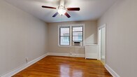 Located at 3221 Connecticut Ave in Washington, DC, this two-bedroom, one-bathroom residence offers a practical and well-designed layout across a single floor. Warm hardwood flooring runs throughout the bedrooms and hallways, lending a classic character to the space. Both bedrooms are well-proportioned, each featuring ceiling fans with light fixtures, large windows that invite natural light, and window-mounted AC units for year-round comfort. The primary bedroom is notably spacious, offering ample room for furnishings. A cast-iron radiator in the second bedroom adds a charming, vintage touch consistent with the building's classic architecture. Neutral gray walls throughout create a clean, versatile backdrop. The kitchen stands out with rich cherry-toned cabinetry, granite-style countertops, a stainless steel sink, and black appliances including a full-size refrigerator, all set atop tile flooring. The bathroom features a full soaking tub with chrome fixtures and a windowed surround finished in crisp white. Connecting hallways provide efficient circulation between rooms. The overall ambiance is cozy yet functional, blending traditional architectural details with practical modern updates suited for urban DC living.