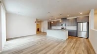 Located at 7501 Jefferson St in Albuquerque, NM, this modern two-story unit offers a thoughtfully designed layout across two levels. The main living floor hosts an expansive open-concept kitchen and living area bathed in natural light, with light-toned wood-style flooring that flows seamlessly throughout. The kitchen is a standout feature, showcasing sleek gray flat-front cabinetry extending to the ceiling, white subway tile backsplash, white quartz countertops, stainless steel appliances, and a central island with pendant lighting — ideal for cooking and entertaining. The living area connects to an outdoor-facing sliding glass door dressed with vertical blinds, allowing abundant light and exterior views. The generously sized bedroom features multiple windows, a ceiling fan, and direct access to a spacious walk-in closet fitted with wire shelving. The full bathroom is well-appointed with gray vanity cabinetry, a large mirror, recessed lighting, and a glass-enclosed walk-in shower with tile surround. A dedicated laundry area and an attached private garage with an automatic opener complete the unit, offering exceptional convenience and functionality in a clean, contemporary package.