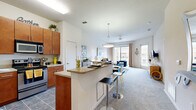 This 1-bedroom, 1-bathroom residence is thoughtfully designed to maximize both comfort and functionality across a single floor. The open-concept layout seamlessly connects the kitchen and living room, creating an inviting and cohesive living space. The kitchen is outfitted with warm-toned wood cabinetry, stainless steel appliances including a refrigerator, range, and microwave, and granite-style countertops that extend to a breakfast bar with bar seating — ideal for casual dining or entertaining. Tile flooring grounds the kitchen, while the living area transitions to plush carpeting. The living room is bright and airy, featuring a ceiling fan, large sliding glass doors, and additional windows that flood the space with natural light and offer outdoor views. The bedroom is a comfortable retreat, carpeted and well-lit by a generously sized window with vertical blinds. It provides ample space for a full furniture arrangement. The bathroom includes a full tub-shower combination with tile surround, a vanity with wood cabinetry, and tile flooring. Throughout the residence, neutral wall tones and consistent finishes create a clean, modern aesthetic well-suited for everyday living.