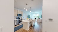 Located in Orlando, FL, this well-appointed 2-bedroom, 3-bathroom residence offers a thoughtfully designed single-floor layout with a clean, contemporary aesthetic. The open-concept kitchen and living area serves as the heart of the home, featuring light wood-grain cabinetry that extends floor to ceiling, white quartz countertops, stainless steel appliances, and a central island with seating — ideal for casual dining or entertaining. Pendant lighting above the island adds a refined touch. The living room is bathed in natural light through large windows framing views of lush palm trees, and a ceiling fan enhances the airy feel. Light wood-tone flooring flows seamlessly throughout the space. The primary bedroom is a generous retreat with outdoor views, warm natural light, and ample space for a full furniture arrangement. The bathrooms are finished with marble-style tile surrounds, light wood vanities, and white quartz countertops, maintaining a cohesive, upscale look. Two dedicated closets provide practical storage. The overall ambiance is bright, modern, and inviting — a polished living experience in the heart of Central Florida.