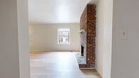 Located at 514 Semple St in Pittsburgh's Oakland neighborhood, this single-floor unit offers three bedrooms and one bathroom across a well-organized layout. The living room serves as the centerpiece of the home, highlighted by a striking full-height exposed brick fireplace with a classic wood mantel and light hardwood flooring that adds warmth and character to the space. A window allows natural light to brighten the room. The kitchen is functional and efficient, featuring warm oak cabinetry, dark granite-style countertops, a peninsula with open shelving, and white appliances including a gas range and refrigerator. A skylight and recessed lighting illuminate the space, while an exposed brick accent wall ties the kitchen visually to the living area. The three bedrooms are carpeted for comfort; the primary bedroom is generously sized and includes a closet, while the additional bedrooms offer natural light through windows. The bathroom is finished with full-height tile surround around the tub-shower combination, accented by a decorative mosaic tile border. The unit is connected by a central hallway and entrance, creating a straightforward and accessible floor plan throughout.