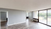 This single-floor residence offers a clean, modern aesthetic throughout, characterized by cool grey walls, white trim, and durable wood-style flooring that flows seamlessly across the main living areas. The open living room is generously proportioned, bathed in natural light through floor-to-ceiling windows and a sliding glass door that opens to a private balcony overlooking outdoor greenery. A wall-unit HVAC system provides individualized climate control.

The kitchen has been thoughtfully updated with crisp white shaker-style cabinetry, granite-look countertops, a subway tile backsplash, and a full suite of stainless steel appliances including a refrigerator, dishwasher, and range. The layout maximizes counter and storage space efficiently.

The bedrooms are well-sized, each finished with the same grey palette and wood-style flooring, with one bedroom featuring carpet. Several rooms include wall-unit climate control and ample natural light from large windows fitted with horizontal blinds. One bedroom benefits from access to a walk-in closet with built-in shelving.

The bathroom is neatly updated with marble-style tile surrounding the tub and shower, complemented by wood-style flooring and clean white fixtures. The overall ambiance is bright, neutral, and move-in ready.
