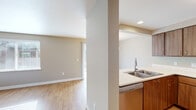 This single-floor residence offers a thoughtfully designed layout with a clean, neutral aesthetic that creates a bright and welcoming atmosphere throughout. The open kitchen is a functional highlight, featuring warm wood cabinetry, light countertops, stainless steel appliances including a range and refrigerator, a double basin sink, and a dishwasher. The kitchen opens toward the dining and living areas, promoting a connected and sociable flow. The living room is generously proportioned, bathed in natural light through large windows with blinds, and finished with light hardwood-style flooring that extends throughout the main living spaces. A dedicated dining area sits adjacent, accented by a chandelier overhead. The bedrooms offer a comfortable retreat, with soft carpet flooring and multiple windows providing ample natural light and outdoor views. Two full bathrooms serve the residence; one features a tub-shower combination, wood-tone vanity, and hardwood-style flooring, while the second includes a single-sink vanity with matching cabinetry and in-unit laundry access. Neutral wall tones, crisp white trim, and consistent warm-toned flooring lend the space a cohesive and move-in-ready character throughout.
