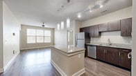 Located at 1415 N Main Ave in San Antonio, Texas, this 2-bedroom, 1-bathroom residence offers a well-designed single-floor layout with a cohesive, modern aesthetic throughout. The open-concept kitchen and living area serves as the heart of the home, featuring rich dark wood cabinetry, granite countertops, stainless steel appliances, and a large central island with pendant lighting above. Wood-style plank flooring extends through the kitchen and living room, adding warmth and continuity to the space.

The living room is bright and airy, with large windows dressed in horizontal blinds that allow ample natural light, complemented by a ceiling fan overhead. Both bedrooms are generously sized, finished with plush wall-to-wall carpeting, ceiling fans, and windows that bring in natural light. The spacious primary bedroom connects to a dedicated walk-in closet with wire shelving for organized storage.

The full bathroom is well-appointed with large-format tile flooring, a dark wood vanity with a granite countertop, a wall mirror, and a tub-shower combination. A dedicated closet is accessible directly from the bathroom, adding convenience. The neutral color palette of warm beige tones throughout the entire residence creates a clean, inviting ambiance suitable for a variety of lifestyles.