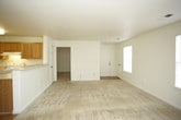This single-story residence offers a straightforward and functional layout designed for comfortable everyday living. The open living area is generously sized, featuring neutral beige carpeting, light-toned walls, and multiple windows fitted with horizontal blinds that allow ample natural light to fill the space. A glass-paneled door provides additional brightness and access from the living room. The kitchen is positioned adjacent to the living area and is separated by a breakfast bar counter. It is outfitted with warm oak-toned cabinetry — both upper and lower — offering substantial storage, along with white appliances including an electric range with a range hood, a dishwasher, a stainless steel sink, and light-colored laminate countertops. Durable wood-look flooring runs throughout the kitchen. The two bedrooms are carpeted and bright, each featuring windows with blinds and standard six-panel doors. One bedroom benefits from a dual-window arrangement, enhancing natural light. The two bathrooms are finished with tile-look flooring and warm wood-toned vanity cabinetry paired with white countertops. One bathroom includes a shower-tub combination, while the other features a single vanity with a large mirror and a well-lit vanity fixture above. Overall, the space presents a clean, neutral palette throughout.