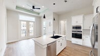 Located at 900 New Day Avenue in Montgomery, Texas, this thoughtfully designed 2-bedroom, 2-bathroom residence offers a clean, modern aesthetic across a single floor. Wood-look tile flooring runs throughout, providing a warm yet low-maintenance foundation for every room.

The open-concept kitchen serves as the heart of the home, anchored by a central island with a curved quartz countertop, an undermount black sink, and sleek pendant lighting overhead. White shaker cabinetry with matte black hardware lines the walls, complemented by stainless steel appliances including a French door refrigerator, double wall ovens, and a dishwasher. A tray ceiling with a ceiling fan and French doors connects the living area to a private outdoor space, filling the room with natural light.

The bedrooms are bright and well-proportioned, each featuring large windows that frame views of the surrounding neighborhood. Both rooms offer access to dedicated closets, with the primary suite including a well-appointed bathroom featuring white cabinetry with quartz countertops. A glass-enclosed walk-in shower with floor-to-ceiling marble-look tile and matte black fixtures adds a refined, spa-like quality. A stacked washer/dryer unit is conveniently tucked within the unit. The overall palette of soft whites and warm neutrals creates a cohesive, move-in-ready atmosphere.
