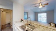 This single-floor residence offers a practical and well-organized layout designed for comfortable everyday living. The open-concept kitchen is outfitted with white cabinetry, light granite-style countertops, a stainless steel sink with a pull-down faucet, a full suite of white appliances including a coil-element range with overhead ventilation, and a full-size refrigerator. A raised breakfast bar visually connects the kitchen to the living area, which features plush wall-to-wall carpeting and a ceiling fan with a light fixture. A sliding glass door in the living area is fitted with vertical blinds and provides access to an outdoor space, allowing natural light to fill the room. The bedrooms are spacious and carpeted, each with neutral-toned walls, and one features a window overlooking a green outdoor setting. The bathroom includes a tub-shower combination, a vanity with storage, and wood-look vinyl flooring, with a sliding closet door adjacent to the entry. Throughout the space, clean white walls, consistent neutral finishes, and functional design elements create a bright, move-in ready environment suited for a range of lifestyles.
