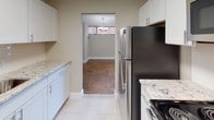 This single-floor unit is defined by its distinctive parquet wood flooring, which extends throughout the living spaces and bedroom, adding warmth and a timeless aesthetic to the interior. The open living and dining area is generously proportioned, bathed in natural light through large windows dressed with vertical blinds, and features a sliding door that provides access to an outdoor area. A textured ceiling and neutral wall tones complete the understated, classic look of these shared spaces.

The kitchen has been thoughtfully updated with crisp white cabinetry, light granite countertops, and stainless steel appliances including a full-size refrigerator and range. Light-toned tile flooring in the kitchen provides a clean contrast to the adjoining living areas, and a pass-through opening connects the kitchen directly to the dining space, enhancing the sense of openness and flow.

The bedroom is well-sized, continuing the parquet flooring, and includes both a standard closet and a dedicated walk-in closet, offering ample storage. The full bathroom is finished with large-format, light grey subway-style wall tiles surrounding a soaking tub and shower combination, complemented by chrome fixtures and a clean white toilet, creating a bright and functional space.