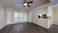 Located at 11710 Parliament St in San Antonio, TX, this single-floor unit offers a thoughtfully designed open-concept layout that seamlessly connects the living and kitchen areas. Rich, dark hardwood-style flooring flows throughout the main living spaces, complemented by warm neutral walls and crisp white trim. Crown molding and ceiling fans add a polished touch to both the living room and adjacent areas.

The living room is bright and inviting, benefiting from large windows that allow generous natural light to fill the space. Built-in shelving provides practical storage alongside the main entry door, which leads to an outdoor area with exterior views.

The kitchen is efficiently laid out in a galley style, featuring white cabinetry, dark granite-style countertops, and a suite of black appliances including a refrigerator, range, microwave, and dishwasher. A peninsula counter creates a natural divide between the kitchen and the living area.

The bedroom is carpeted for comfort and includes a ceiling fan, offering a quiet retreat from the main living space. The unit includes two bathrooms: one with a full tub-shower combination with white tile surround and hardwood-style flooring, and a second featuring a glass-door walk-in shower with tile walls. Tile flooring is present at the entryway, completing this well-appointed and functional home.