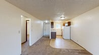 Located at 1550 Q St in Springfield, Oregon, this 2-bedroom, 1-bathroom unit offers a practical single-floor layout designed for comfortable everyday living. The combined living room and kitchen area forms the heart of the unit, where carpet transitions to tile flooring as the spaces meet. The living room features a sliding glass door that fills the room with natural light and provides direct outdoor access. The kitchen is equipped with dark wood cabinetry, a white refrigerator, an electric range, and a dishwasher, all set against light tile flooring and complemented by a window that brings in additional natural light. A hallway connects the main living areas to the two bedrooms and the bathroom. Both bedrooms are carpeted and feature textured ceilings, with the second bedroom offering a closet with bi-fold doors and a window with outdoor views. The primary bedroom includes a closet and its own window. The full bathroom is finished with tile flooring, a wood-toned vanity with a light countertop, and a full tub-shower combination. Throughout the unit, textured ceilings and neutral wall tones create a clean, understated aesthetic.