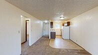 Located at 1550 Q St in Springfield, Oregon, this 2-bedroom, 1-bathroom unit offers a practical single-floor layout designed for comfortable everyday living. The combined living room and kitchen area forms the heart of the unit, where carpet transitions to tile flooring as the spaces meet. The living room features a sliding glass door that fills the room with natural light and provides direct outdoor access. The kitchen is equipped with dark wood cabinetry, a white refrigerator, an electric range, and a dishwasher, all set against light tile flooring and complemented by a window that brings in additional natural light. A hallway connects the main living areas to the two bedrooms and the bathroom. Both bedrooms are carpeted and feature textured ceilings, with the second bedroom offering a closet with bi-fold doors and a window with outdoor views. The primary bedroom includes a closet and its own window. The full bathroom is finished with tile flooring, a wood-toned vanity with a light countertop, and a full tub-shower combination. Throughout the unit, textured ceilings and neutral wall tones create a clean, understated aesthetic.