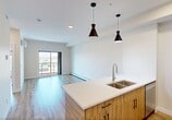Located at 150 Edgemont Road NW in Edmonton, Alberta, this thoughtfully designed one-bedroom, one-bathroom unit offers a contemporary open-concept layout finished with light hardwood-style flooring throughout. The kitchen serves as a central focal point, featuring a large island with a quartz countertop and double undermount sink, complemented by stainless steel appliances including a refrigerator, electric range, and built-in microwave. A mix of warm wood-toned and crisp white cabinetry adds visual contrast, while black pendant lighting lends a modern touch. The kitchen flows seamlessly into the bright living room, which is anchored by a sliding glass door opening onto a private balcony with open views of the surrounding Edmonton neighbourhood. The bedroom is a comfortable size with a large window that allows generous natural light and city views, and features a sliding-door closet for ample storage. A versatile den provides additional flexible living space. In-suite stacked laundry is conveniently tucked within its own dedicated area. The bathroom includes a full soaker tub and shower combination with brushed nickel fixtures. Baseboard heating runs throughout, and a barn-style sliding door adds a stylish architectural detail near the entryway.