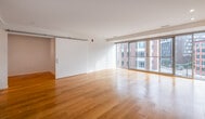 This single-floor unit showcases a clean, contemporary design characterized by crisp white walls, recessed lighting, and warm hardwood flooring that runs consistently throughout the living spaces. The open-concept layout connects the kitchen and living areas seamlessly, creating a cohesive and functional flow.

The kitchen is thoughtfully appointed with floor-to-ceiling white gloss cabinetry, a stainless steel undermount sink, a gas cooktop, a wall oven, and a full-size refrigerator. Ample counter space and abundant upper and lower storage make it both practical and visually refined.

The living area is a standout feature of the unit, anchored by expansive floor-to-ceiling sliding glass doors that open to a balcony and frame dynamic urban views of the surrounding cityscape. Natural light floods the space, enhancing the bright, airy atmosphere.

A barn-style sliding door adds a modern architectural detail, separating spaces while maintaining an open feel. Additional rooms offer generous proportions, white walls, and hardwood floors, providing versatile living arrangements. The bathroom features large-format neutral tiles, a soaking tub with an overhead shower, and chrome fixtures, delivering a clean and functional aesthetic throughout.