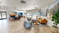Located at 4400 Montgomery Blvd NE in Albuquerque, New Mexico, this single-floor community facility offers a well-appointed and thoughtfully designed space that blends functionality with Southwest-inspired style. Light hardwood flooring runs throughout, unifying the distinct areas while lending a clean, contemporary feel.

The open lounge and reception area serves as the heart of the space, bathed in natural light from expansive floor-to-ceiling sliding glass doors and large windows that frame views of the surrounding landscape. Comfortable seating arrangements — including a cognac leather sofa, modern accent chairs, and round coffee tables — create an inviting atmosphere. Bold large-format artwork depicting desert landscapes, agave plants, and scenic Southwest vistas adorn the walls, reinforcing a strong regional identity.

A dedicated office area features a well-equipped workstation, ample file storage, and high angled ceilings that add volume and visual interest. A compact kitchenette with teal cabinetry and decorative patterned tile backsplash provides a charming utilitarian nook.

The fitness center is equipped with a multi-functional cable machine, elliptical trainer, stationary bike, and treadmill, all set within a bright, airy room accented by linear pendant lighting and natural light from transom windows. Together, these areas create a versatile and welcoming community hub.