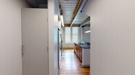 Located at 3300 Clipper Mill Rd in Baltimore's historic Clipper Mill neighborhood, this two-floor loft-style unit blends industrial character with modern finishes. The main floor hosts an open-plan kitchen and living area, where rich, reclaimed hardwood floors extend throughout the space. The kitchen is well-appointed with warm wood cabinetry, dark granite countertops, stainless steel appliances including a refrigerator, electric range, and microwave, and a central island with a sink — all beneath an exposed beam ceiling with integrated lighting that reinforces the industrial aesthetic. Large windows invite generous natural light into the living area, complementing the warm tones of the hardwood floors and crisp white walls. The bathroom features large-format tile flooring, a warm wood vanity with dark granite countertop, and a separate shower enclosure. A staircase with step lighting leads to the upper loft level, which features carpeted flooring, exposed wooden roof trusses, and glass panel railings — offering a dramatic architectural detail and an adaptable space for a bedroom or home office. The two-level layout maximizes the functionality of the overall footprint, making this a distinctive and well-designed urban living space.