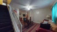 Located in Atlanta, GA, this two-floor home offers a practical and comfortable layout across its levels. The living room serves as the heart of the main floor, featuring warm hardwood flooring, a ceiling fan with light fixture, and a textured ceiling. A staircase connects both floors, and the open feel of the space is enhanced by neutral wall tones. The kitchen is well-equipped with white cabinetry offering ample storage, a black range, double-basin sink, and laminate tile flooring. A nearby dining area accommodates a round glass-top table and is accented by decorative wall art, making it a pleasant space for meals. The bathroom features white subway tile wainscoting, a vanity with cabinet storage, and a mirrored medicine cabinet. The primary bedroom includes rich hardwood flooring, windows with curtains providing natural light, and a textured ceiling. An additional bedroom is a clean, open room with hardwood floors, a window with blinds, and a window-mounted air conditioning unit. Throughout the home, hardwood-style flooring runs consistently, contributing to a cohesive and easy-to-maintain interior. The layout across two floors provides a clear separation of living and private spaces.