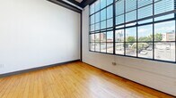 Unit 304 at 101 E Sixth St is an urban loft in downtown Winston-Salem, NC, blending industrial character with modern finishes. Warm hardwood floors and soaring ceilings run throughout the open-concept living and kitchen area, where exposed ductwork and structural elements add an authentic loft aesthetic. The kitchen features dark wood cabinetry, granite countertops, stainless steel appliances, and pendant lighting. Large factory-style windows flood the bedrooms with natural light and offer city views. Both bathrooms are finished with granite vanities, dark cabinetry, and large-format tile flooring. The primary bedroom includes a dedicated closet.