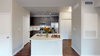This single-story residence offers a thoughtfully designed layout that maximizes its compact footprint. The kitchen serves as a central highlight, featuring dark espresso-toned cabinetry, stainless steel appliances including a range, built-in microwave, and French door refrigerator, complemented by a white subway tile backsplash and light quartz countertops. A curved peninsula island with an undermount sink provides additional prep space and casual seating, creating a natural transition into the living area. Rich hardwood-style flooring flows throughout the main living and kitchen spaces, adding warmth and contrast to the neutral gray walls.

The bedroom is a comfortable, carpeted retreat equipped with a ceiling fan, multiple windows dressed with white blinds, and ample natural light. The full bathroom is finished with dark cabinetry matching the kitchen, a white quartz vanity top, a tub-shower combination with neutral tile surround, and chrome fixtures throughout. A dedicated closet adds practical storage. The overall ambiance is modern and cohesive, with a clean, neutral palette and consistent finishes that lend the space a polished, move-in-ready appeal.