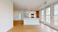Located at 200 Townsfolk Alley in Penfield, NY, this thoughtfully designed 2-bedroom, 1-bathroom residence offers a clean, modern aesthetic across a comfortable single-floor layout. The entry foyer welcomes you with light bamboo-style hardwood flooring, crisp white walls, and a smart keypad entry door, with a utility room conveniently accessible nearby.

The open-concept kitchen and living area serves as the heart of the home. The kitchen is outfitted with white upper cabinetry, warm wood-toned lower cabinets, stainless steel appliances including a French door refrigerator and built-in microwave, and a large center island with a white quartz countertop and undermount sink. Track lighting overhead and large windows allow generous natural light to fill the space, offering pleasant outdoor views.

The bathroom features a wood-tone vanity with a white countertop, a framed mirror, and a glass-enclosed walk-in shower, all carried through on the same light hardwood-style flooring. Both bedrooms are carpeted for comfort, with the primary bedroom providing a generous footprint, and both rooms benefiting from large windows that bring in ample daylight. Two closets provide practical storage throughout. The overall ambiance is bright, clean, and contemporary.