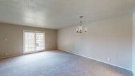 This single-floor residence offers a thoughtfully laid-out living space with a clean, neutral aesthetic throughout. The main living and dining area is generously proportioned, featuring soft wall-to-wall carpeting, a textured ceiling, and an elegant brass chandelier as a focal point. French doors with slatted blinds invite natural light and provide access to the outdoors, creating an airy, open atmosphere.

The kitchen has been updated with crisp white shaker-style cabinetry, sleek white countertops, and a subtle gray subway tile backsplash. A stainless steel double-basin sink sits beneath a window with blinds, and the space is well-equipped for everyday use.

The bedrooms are comfortably sized, each carpeted and brightened by windows with blinds that allow natural light to filter in. The rooms maintain a consistent warm, neutral palette that lends a calm and versatile character to the space.

A hallway connects the living areas to the private spaces, with wood-look flooring near the entryway providing a practical and attractive transition zone. The bathroom is finished with a white tiled tub-and-shower combination, a white vanity, and warm wood-look flooring, all accented by brushed nickel fixtures. Overall, this residence presents a well-maintained, move-in-ready interior with consistent finishes throughout.