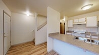 Located at 3349 SE Summerfield Dr in Corvallis, Oregon, this two-story residence offers a practical and well-organized layout across two levels connected by a carpeted staircase. The main level features wood-look laminate flooring throughout, lending a clean and cohesive aesthetic to the common areas. The kitchen is equipped with white cabinetry, a double-basin stainless steel sink, laminate countertops, a white electric range, and a full-size refrigerator. A peninsula counter opens toward the adjacent living area, creating an efficient flow between cooking and living spaces. The main level also includes a half bathroom with a vanity and wood-look flooring. The living room is generously proportioned, featuring sliding glass doors that invite natural light and provide outdoor views of the surrounding greenery. Upstairs, the bedrooms are carpeted for comfort and feature neutral walls and windows that allow natural light. One bedroom offers a pleasant view of mature trees outside. A full bathroom on the upper level includes a shower-tub combination and wood-look flooring. The upper hallway features a built-in storage unit, adding functional convenience. Throughout the home, the design emphasizes clean lines, light neutral tones, and practical finishes suited for comfortable everyday living.