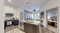 This well-appointed 1-bedroom, 1-bathroom residence offers a cohesive modern design across a single floor. The open-concept kitchen and living area serves as the heart of the home, where a striking kitchen island with granite countertops and dual-tone cabinetry — navy lower cabinets paired with crisp white uppers and gold hardware — takes center stage. Stainless steel appliances, a herringbone tile backsplash, and pendant lighting complete the kitchen's refined aesthetic. The living area flows naturally from the kitchen, featuring warm wood-look flooring, sheer floor-to-ceiling curtains, and a glass door that fills the space with natural light. The bedroom offers a calm, neutral palette with soft carpeting, a window with exterior views, and access to a dedicated walk-in closet outfitted with built-in shelving and hanging rods. The bathroom is elegantly finished with a double granite-topped vanity featuring matching cabinetry and gold hardware, a frameless glass walk-in shower with tile surround, and an illuminated mirror. Throughout the residence, consistent finishes and a neutral color scheme create a cohesive, contemporary ambiance.