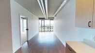 Located at 624 Yale Ave N, Unit 615 in Seattle, WA 98109, this single-floor space sits within the vibrant South Lake Union neighborhood. The open-plan layout offers a clean, versatile canvas well-suited for a variety of professional uses. Rich hardwood flooring runs the length of the space, providing a warm contrast to the exposed concrete ceiling above, which features industrial-style conduit and track lighting that contribute to a modern, loft-like aesthetic. Expansive floor-to-ceiling windows along the far wall flood the interior with abundant natural light and frame sweeping views of the surrounding Seattle cityscape and neighboring rooftops. The clean white walls enhance the brightness and sense of openness throughout. A glass-paneled interior door adds a functional yet stylish partition element near the entry. Built-in cabinetry provides practical storage along one wall. The overall ambiance is modern and airy, combining industrial design elements with polished finishes to create a bright, professional environment ideal for creative or office use.