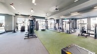 Located at 5704 Ella View in Colorado Springs, CO, this modern fitness center offers a generously sized, single-floor layout designed to accommodate a comprehensive range of workout disciplines. The space features a contemporary architectural design with tiered ceiling details finished in muted gray tones, recessed and linear LED lighting, and large windows that flood the interior with natural light while providing views of the surrounding neighborhood.

The main workout floor is divided into several well-defined zones. A dedicated free weights area houses an extensive dumbbell rack, barbells, and multiple adjustable benches, complemented by full-length wall mirrors that enhance the sense of openness. A robust selection of selectorized strength machines and cable systems is distributed throughout the space, catering to both isolation and compound movements.

A standout feature is the functional training turf zone, surfaced in bright green artificial turf and equipped with battle ropes, a tire, sled equipment, and a rowing machine — ideal for high-intensity functional training. A separate cardio area accommodates spin bikes, treadmills, ellipticals, and a wall-mounted display screen. Ceiling fans ensure consistent air circulation throughout. Additional amenities include a water fountain station and access to adjoining utility rooms, making this a fully equipped, professional-grade facility.
