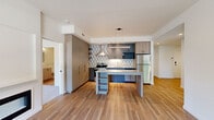 Located at 435 Alexander Loop in Eugene, Oregon, this two-bedroom, two-bathroom residence offers a thoughtfully designed single-level layout with modern finishes throughout. The open-concept kitchen and living area serves as the heart of the home, showcasing warm wood-tone cabinetry, two-tone gray lower cabinets, and a striking geometric-patterned backsplash. A central kitchen island with built-in shelving provides additional prep and storage space, while stainless steel appliances — including a refrigerator, range, and dishwasher — complete the well-appointed kitchen. Pendant lighting and recessed fixtures illuminate the space, and durable wood-style flooring runs throughout the main living areas. A hallway connects the living space to the two bedrooms and bathrooms. The primary bedroom features plush carpeting, a linear fireplace feature, and a large window that allows natural light and outdoor views. The bathrooms are finished with wood-tone vanities, white quartz countertops, round mirrors with black frames, soaking tubs, and wood-style flooring. A dedicated closet provides practical storage. In-unit laundry is also visible, adding convenience to this well-equipped residence.