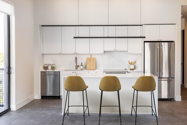 Signature Collection kitchen with white cabinetry, white marbled quartz countertop and backsplash, wine fridge, and upgraded stainless steel appliances - Avalon South Miami Apartments